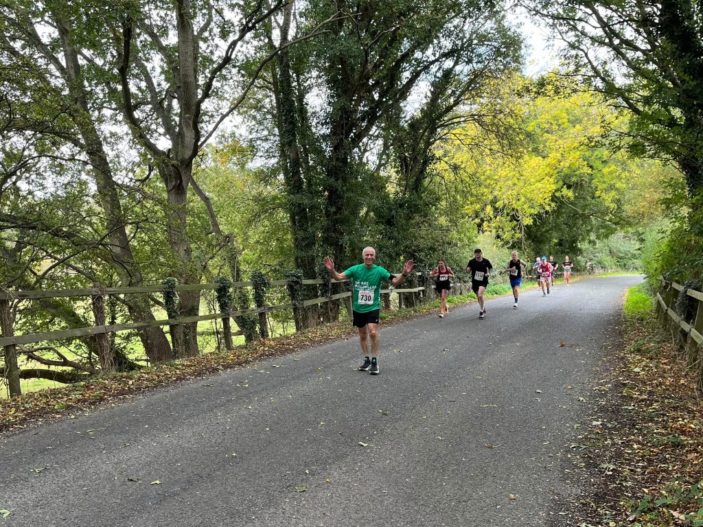 Glynn in a Norfolk Run Collective shirt during a road race, arms outstretched