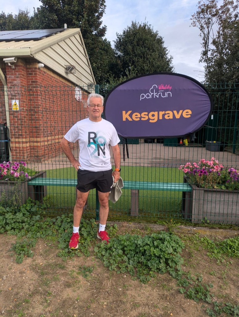 Club runner standing by the Vitality parkrun Kesgrave sign
