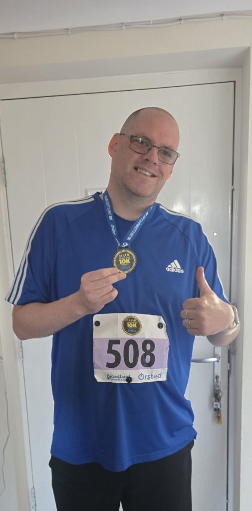 Runner holding an Ørsted Broadland 10K medal, wearing bib 508