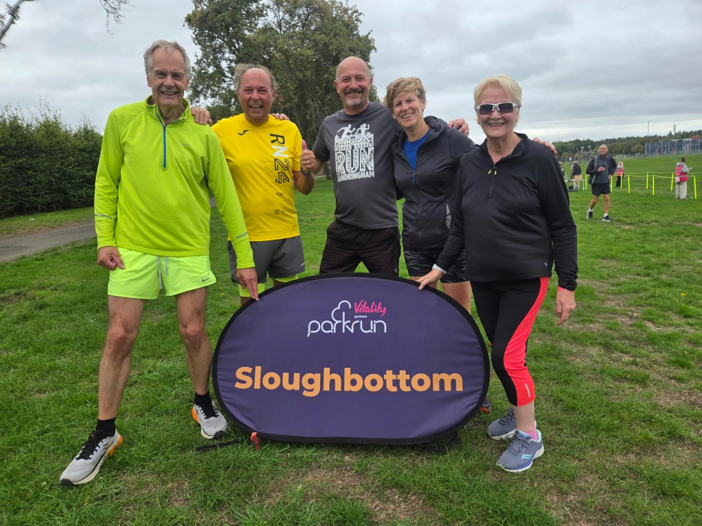Five club runners with the Vitality parkrun Sloughbottom sign