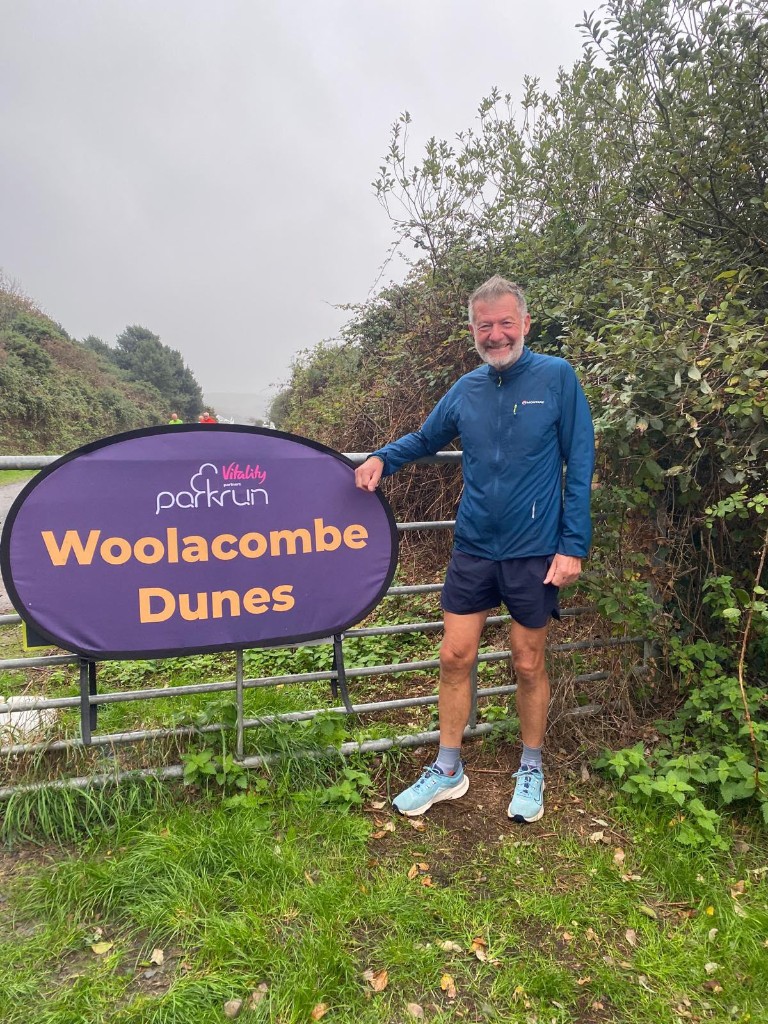 Club runner beside the Vitality parkrun Woolacombe Dunes sign